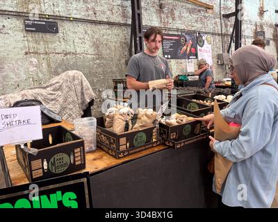 Le vendeur de champignons interagit avec un client au Carriageworks Farmers Market à Sydney, en Australie, avec des boîtes de champignons frais et séchés exposées. Banque D'Images