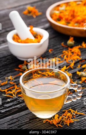 Tasse de thé au calendula, accompagnée de pétales séchés et d'un mortier blanc avec des fleurs de calendula - Calendula officinalis Banque D'Images