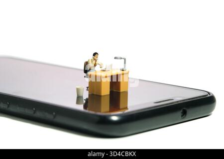 Miniature Tiny People jouet figure photographie. Travaillez où que vous soyez, concept de travailleur mobile. Un siège d'homme d'affaires sur son bureau, au-dessus du smartphone. Isolé sur Banque D'Images