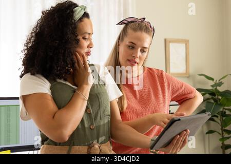 Diverses collègues féminines discutant des détails sur tablette numérique dans le bureau à domicile, avec des plantes en pot Banque D'Images