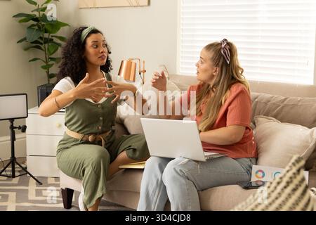 Gestuelle, diverses amies féminines collaborant sur le canapé dans le salon, avec ordinateur portable et pot Banque D'Images