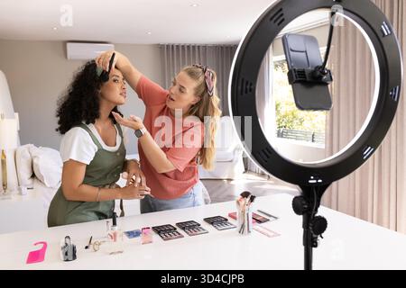 Application de maquillage, diverses amies féminines démontrant tutoriel dans le home studio, avec lumière annulaire Banque D'Images