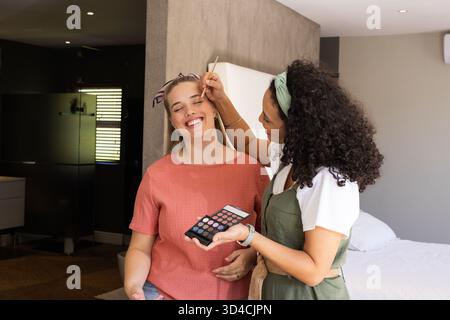 Diverses amies féminines appliquant le maquillage des yeux dans un studio moderne, avec brosse et palette Banque D'Images