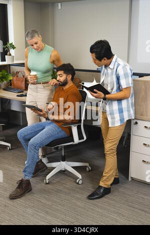Divers collègues discutent du projet autour du bureau dans le bureau, avec tablette et ordinateur portable Banque D'Images