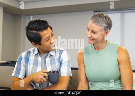 Bavardez divers collègues assis dans la zone de bureau moderne, avec une tasse à café en céramique foncée Banque D'Images