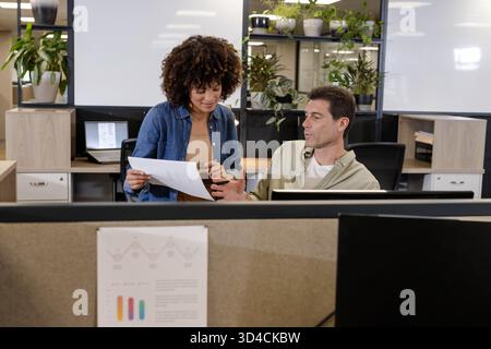 Examen de divers collègues collaborant dans le bureau, avec rapport imprimé, moniteurs, usines Banque D'Images