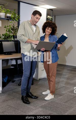 Analyse du rapport divers collègues collaborant dans un bureau ouvert, tenant un ordinateur portable et un ordinateur portable Banque D'Images