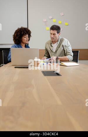 Collaboration de collègues divers examinant des documents dans un bureau moderne, avec un ordinateur portable et des notes adhésives Banque D'Images