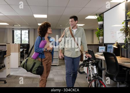 Marcher divers collègues se déplacer dans un bureau ouvert, porter un tapis de yoga et pousser un vélo Banque D'Images