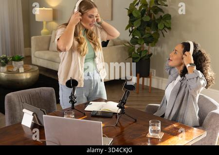 Diverses collègues féminines enregistrant un podcast dans un salon confortable, avec des micros et des écouteurs Banque D'Images
