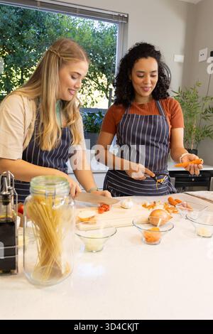 Hacher diverses amies féminines préparant le repas au comptoir dans la cuisine, avec une planche à découper en bois Banque D'Images