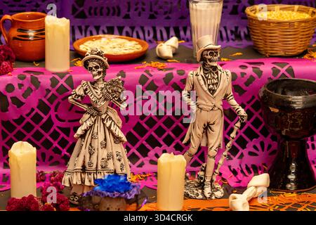 Deux squelettes habillés de blanc et noir, debout sur une table avec des bougies et autres décorations. Fête mexicaine de la tradition des morts, offrandes, nourriture, Banque D'Images