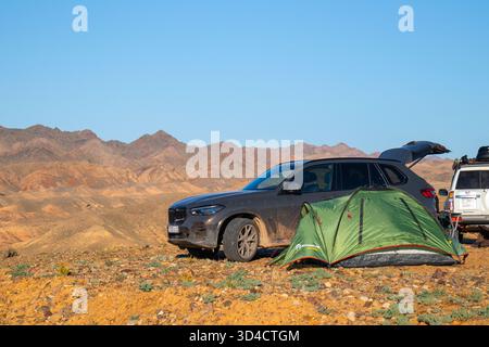Naryn, Kirghizistan - 13 mai 2024 : un VUS BMW X5 G05 de couleur foncée est garé à côté d'une tente verte, avec un VUS Nissan Patrol blanc partiellement visible, dans un Banque D'Images