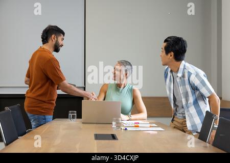 Serrant la main de divers collègues négociant un accord dans une salle de réunion moderne, avec ordinateur portable et documents Banque D'Images