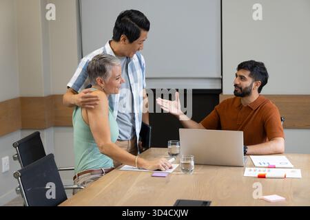 Collaboration de divers collègues examinant des graphiques à table dans le bureau, avec un ordinateur portable et des notes adhésives Banque D'Images