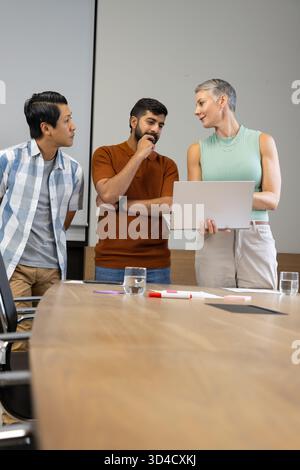 Divers collègues discutant autour de la table de conférence dans la salle de réunion, avec ordinateur portable et papiers Banque D'Images