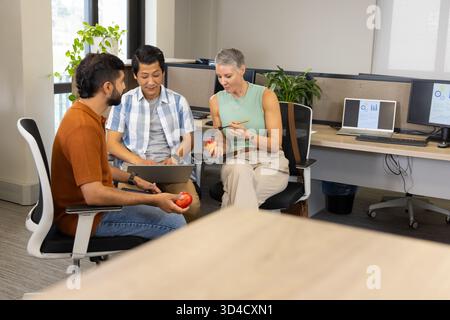 Examen du travail divers collègues assis dans un bureau ouvert, avec ordinateur portable pomme et conteneur de fruits Banque D'Images
