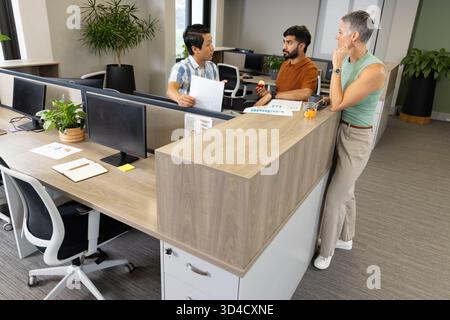 Divers collègues discutent des documents imprimés dans un bureau moderne ouvert, avec pomme et moniteurs Banque D'Images