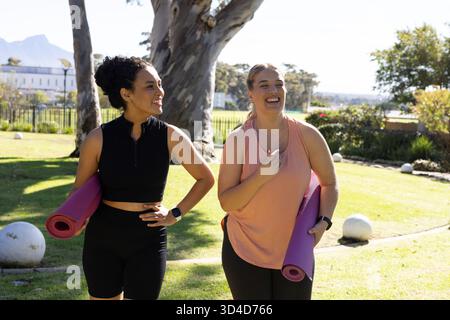 Flâner diverses amies riant dans le parc, porter des tapis de yoga et passer des sculptures en pierre Banque D'Images