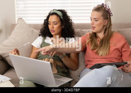 Examen des notes diverses amies féminines assises sur le canapé dans le salon, avec ordinateur portable, tablette, papiers Banque D'Images