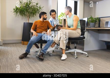 Collaboration de divers collègues examinant la tablette dans un bureau moderne, avec des plantes en pot Banque D'Images