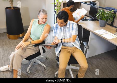Collaborer avec divers collègues assis dans un bureau ouvert, à l'aide d'une tablette numérique et de graphiques Banque D'Images