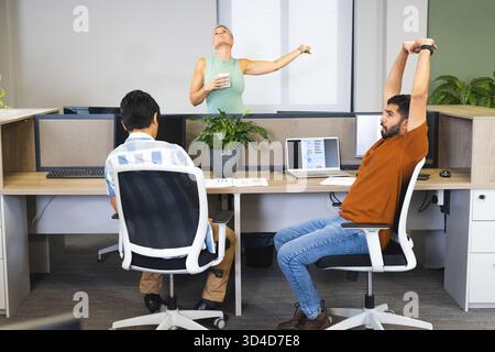 Des employés divers qui se penchent en arrière sur des bureaux ouverts, avec deux moniteurs et une usine Banque D'Images