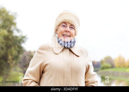 Femme âgée heureuse en manteau chaud et chapeau de fourrure un jour d'automne. Femme d'affaires caucasienne souriante. Portrait féminin à la retraite pour la publicité. Banque D'Images