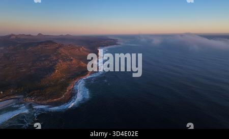 Vue aérienne de la côte accidentée rencontrant le vaste océan sous un ciel doux, de couleur pastel, avec des brumes dansant à l'horizon, Cape Town, Ouest Banque D'Images