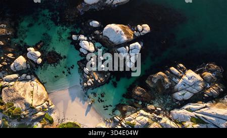 Vue aérienne des rochers massifs rencontrent la mer turquoise, créant un contraste saisissant avec la plage de sable, Cape Town, Western Cape, Afrique du Sud. Banque D'Images
