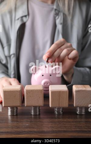 Femme mettant la pièce dans la tirelire à la table en bois, se concentrer sur les cubes vierges et l'argent. Maquette pour le design Banque D'Images