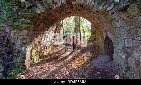 Vue d'une mère et d'un enfant marchant à travers un tunnel voûté en pierre, la lumière du soleil battant le chemin devant, Haddington, Écosse, Royaume-Uni. Banque D'Images