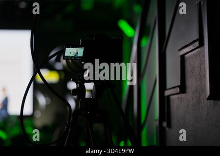 Caméra numérique sans miroir montée sur trépied filmant la présentation dans la salle de conférence avec éclairage professionnel, symbolisant la diffusion en direct, événement vide Banque D'Images