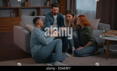 Quatre amis multiethniques avec ordinateur portable choisissant le film en ligne film de cinéma à la maison partie discuter de la livraison de nourriture de commande à l'événement domestique parler à la recherche dedans Banque D'Images