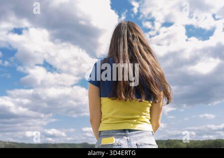 Femme méconnaissable dans un T-shirt jaune et bleu avec ses cheveux vers le bas contre le ciel. Vue de derrière. Fier d'être ukrainien. Tenez-vous avec l'Ukraine. Pour Banque D'Images