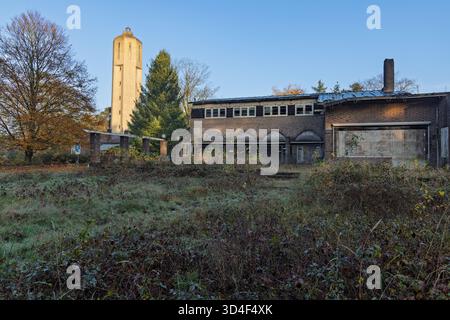 La zone industrielle abandonnée de Radio Kootwijk avec le haut château d'eau et un bâtiment en briques délabré et envahi au premier plan. Banque D'Images