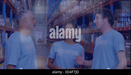 Discuter de trois bénévoles portant des chemises bleu clair dans l'allée de l'entrepôt, près des étagères à palettes Banque D'Images