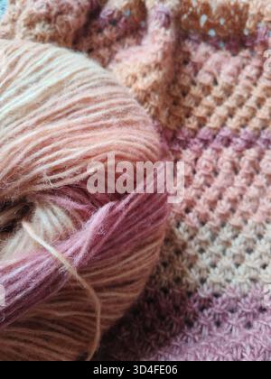 Un gros plan d'une pièce triangulaire tricotée dans des tons oranges chauds est à côté d'une boule de fil Banque D'Images