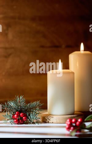 Cozy Christmas Still Life avec deux bougies blanches brûlantes, des branches de pin et des baies de houx rouges Banque D'Images