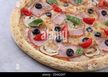 Nourriture, pizza cuite au feu de bois garnie de tranches de jambon fumé, d'olives noires, de champignons sautés, de tomates cerises coupées en deux et de feuilles de basilic frais sur un golde Banque D'Images