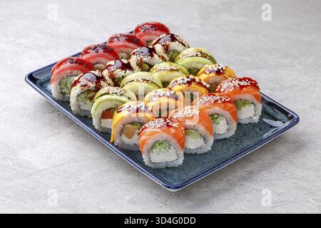 Nourriture, rouleaux de sushi arc-en-ciel vibrants nappés de tranches de saumon, thon, mangue et avocat, farcis de fromage à la crème et de concombre, arrosés de sauce anguille Banque D'Images
