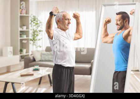 Senior en vêtements de sport fléchissant les muscles du bras devant le miroir et regardant sa version plus jeune Banque D'Images