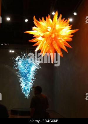 SEATTLE - APR 25, 2025 - deux lustres en verre coloré, un orange et un bleu, sont suspendus au plafond d'une pièce sombre, créant un intéressant Banque D'Images