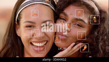 Rire deux femmes adultes pressant les joues ensemble en studio, portant des bandeaux avec des icônes HUD Banque D'Images