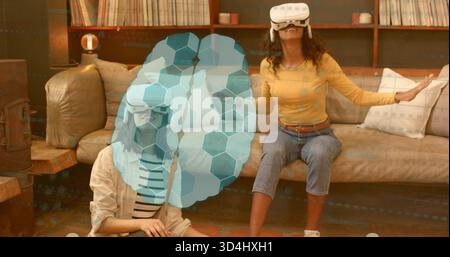 Interagir avec deux femmes portant de la moutarde et des vêtements rayés en utilisant des casques VR à la maison, recouvrement AR Banque D'Images