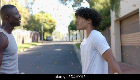 Hommes debout portant un débardeur gris et un T-shirt blanc sur une rue de banlieue, porte de garage, taches orange Banque D'Images