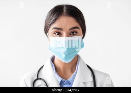Portrait de joyeuse jeune indienne Lady Doctor en masque protecteur et manteau blanc Banque D'Images