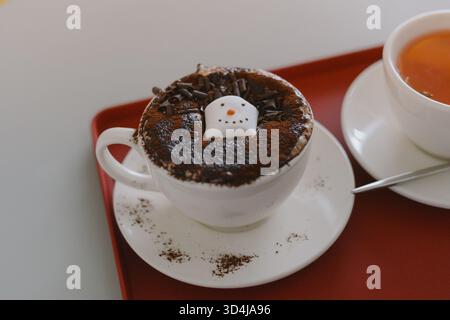 Table de café confortable avec une tasse de chocolat chaud surmontée d'une décoration bonhomme de neige Banque D'Images