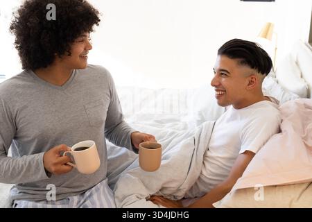 Partageant des tasses de café, divers amis masculins assis sur le lit dans une chambre confortable, avec des tasses en céramique Banque D'Images