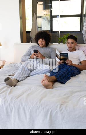 Se prélasser divers amis masculins lisant le livre de poche et vérifiant smartphone dans la chambre, avec tasse à café Banque D'Images